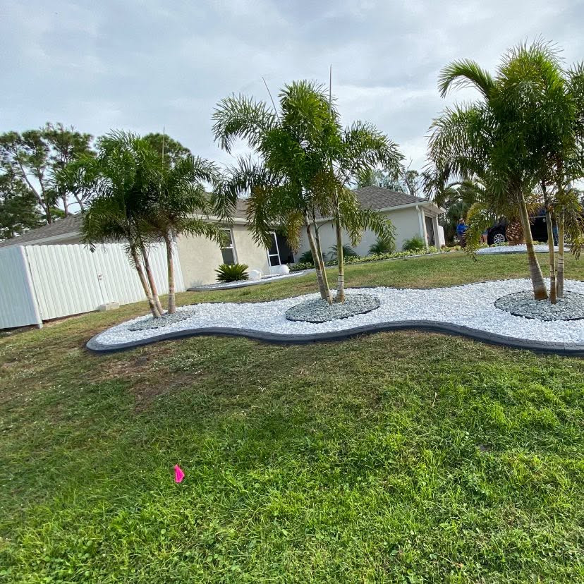 Wavy charcoal curbing enclosing a white rock bed with a row of queen palms
