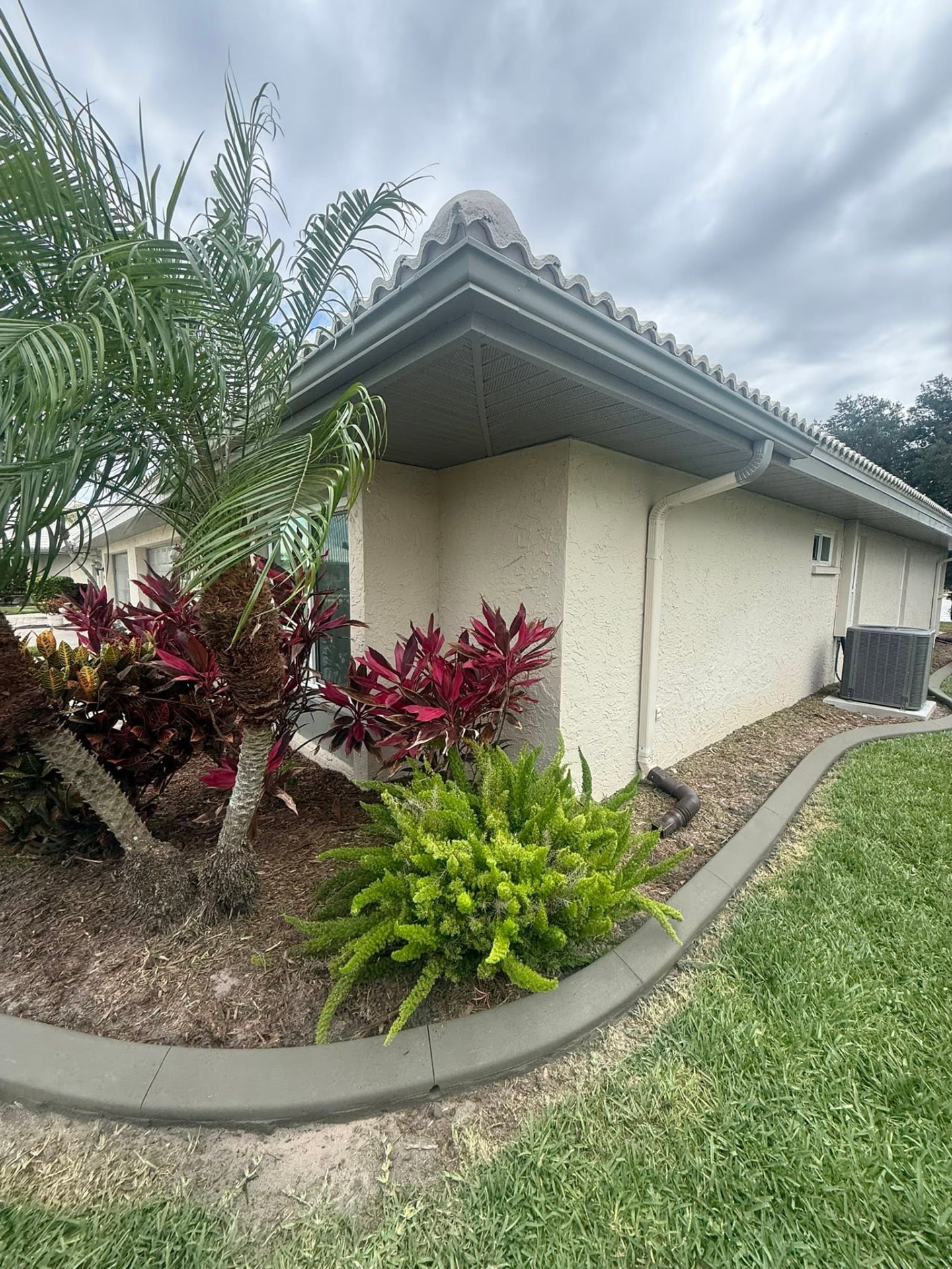 Sweeping gray curb around a tropical croton and palm bed at a home corner