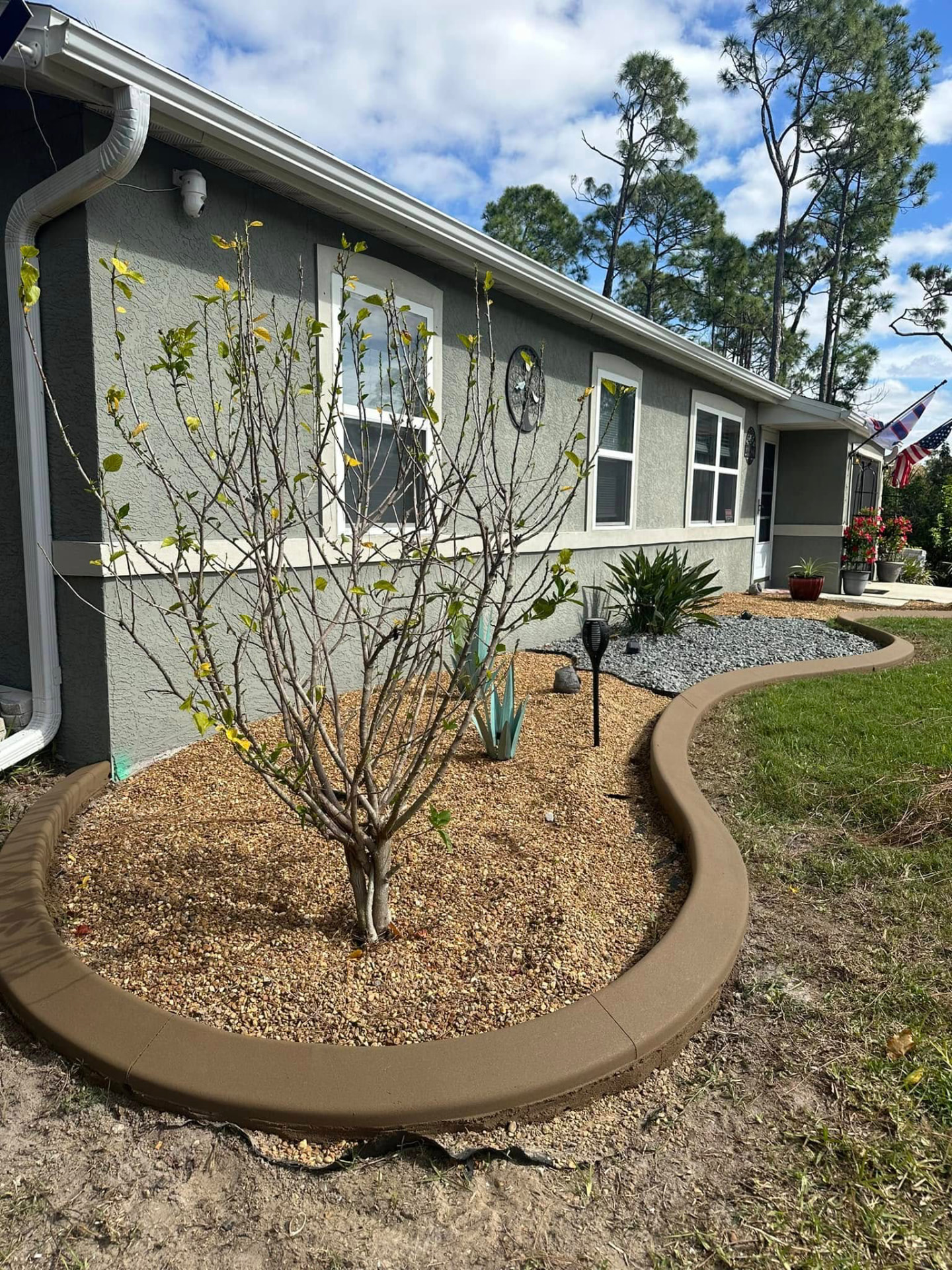 Wavy tan curbing wrapping a pea gravel bed in a front yard