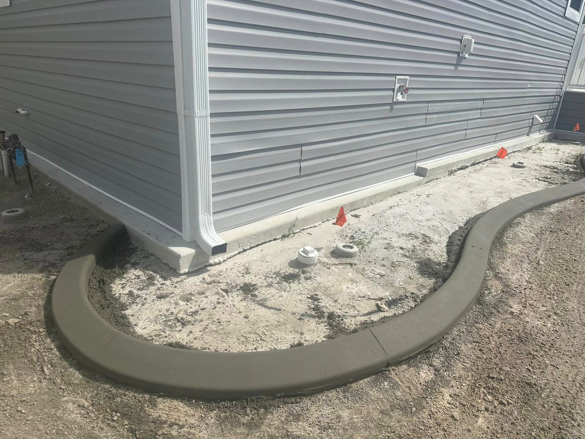 Freshly poured gray curbing curving around a new construction home