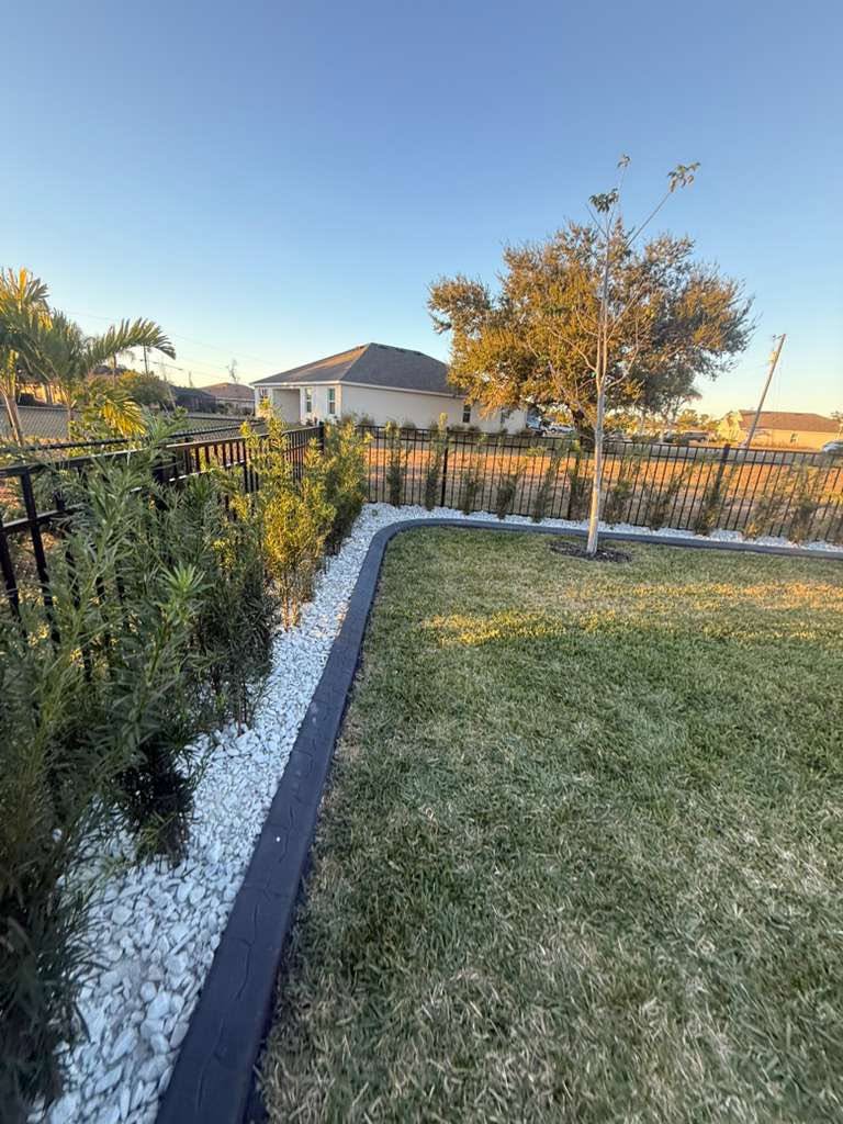 Black curbing separating a white rock privacy hedge bed from the lawn