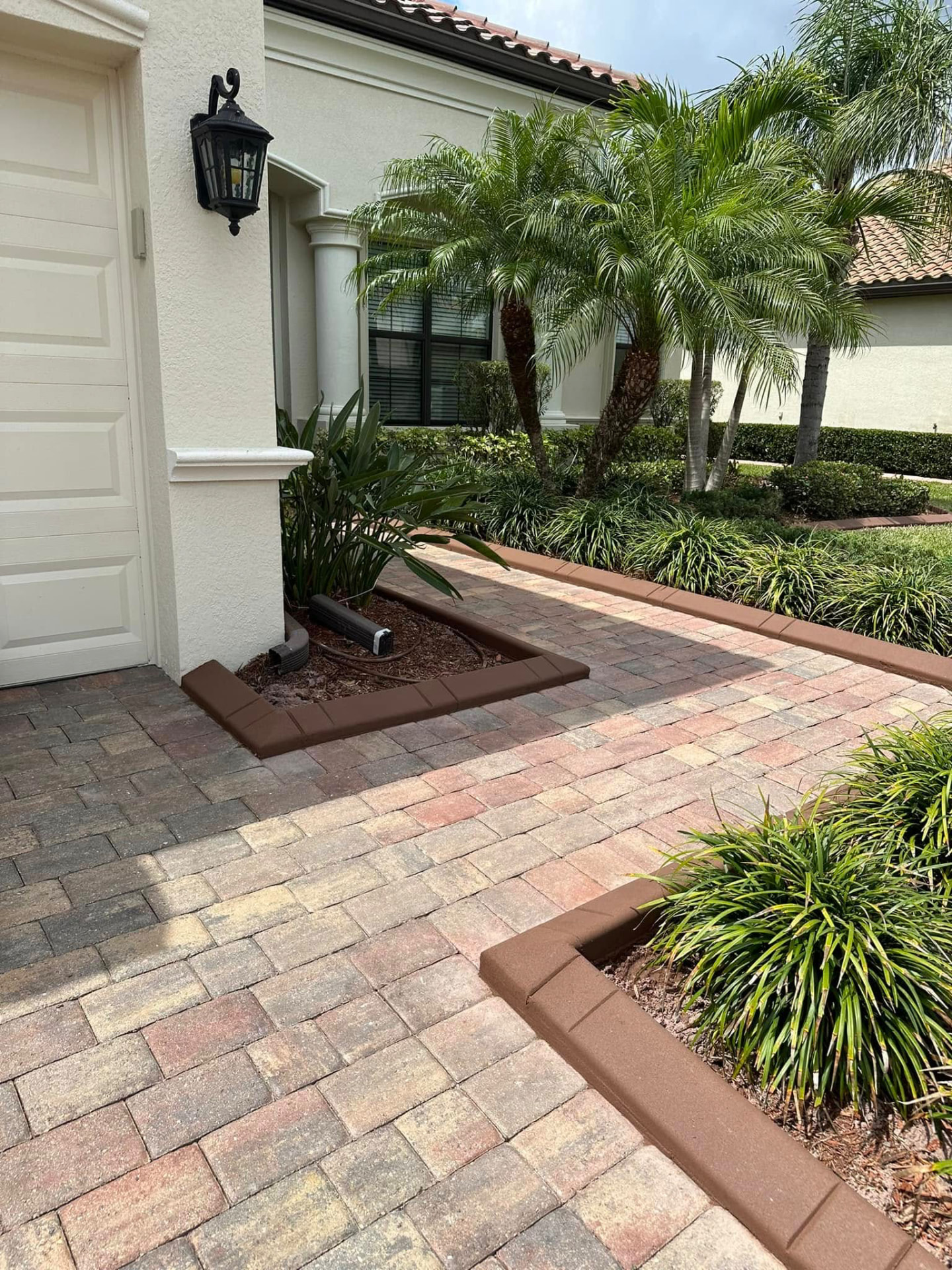 Brown brick-stamped curbing edging a paver driveway and mulch bed at a tile-roof home
