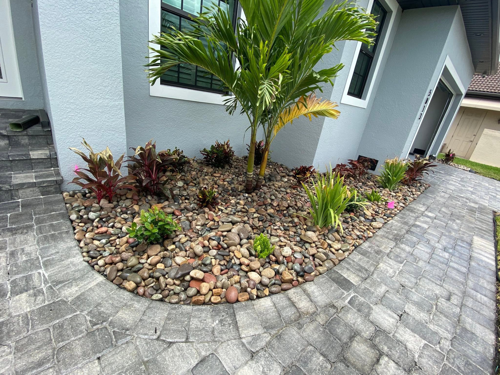 Curved border framing a multicolor river rock bed with crotons at a modern home entry