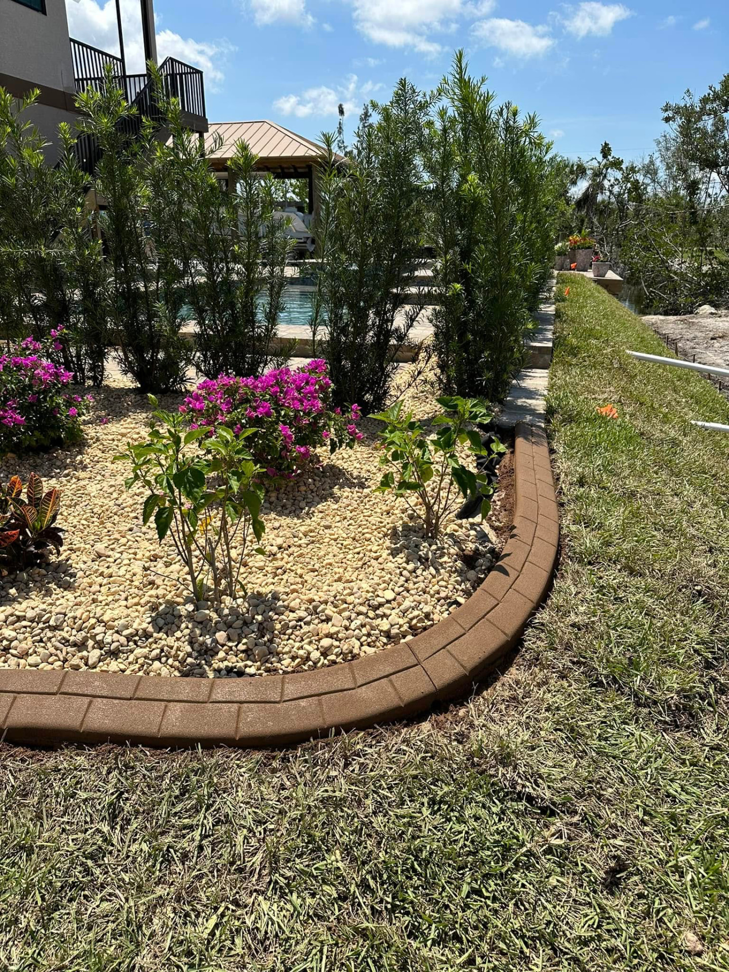 Brick-stamped brown curbing beside a poolside tropical planting bed