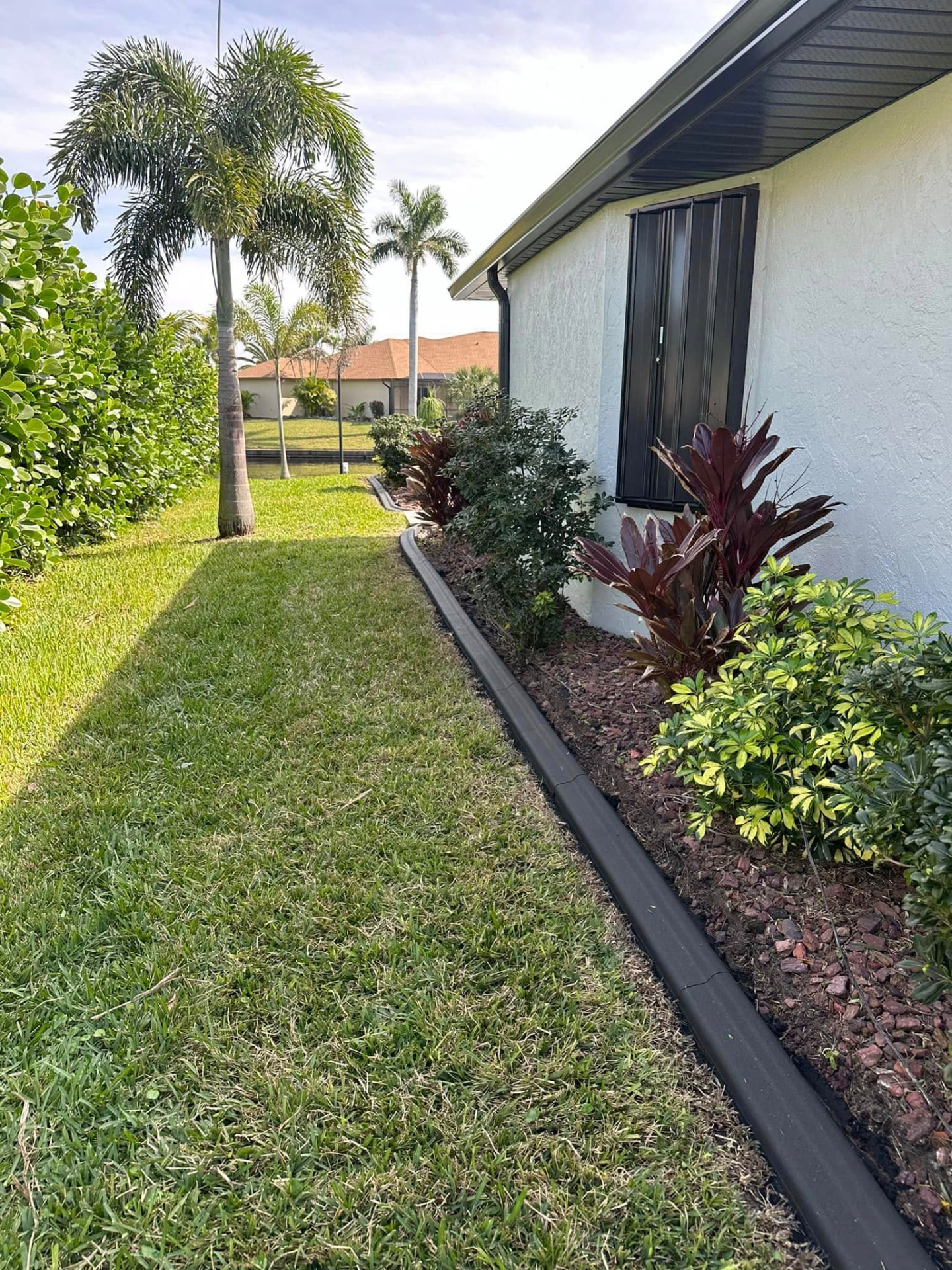 Slim dark curb separating a manicured lawn from a red mulch planting bed