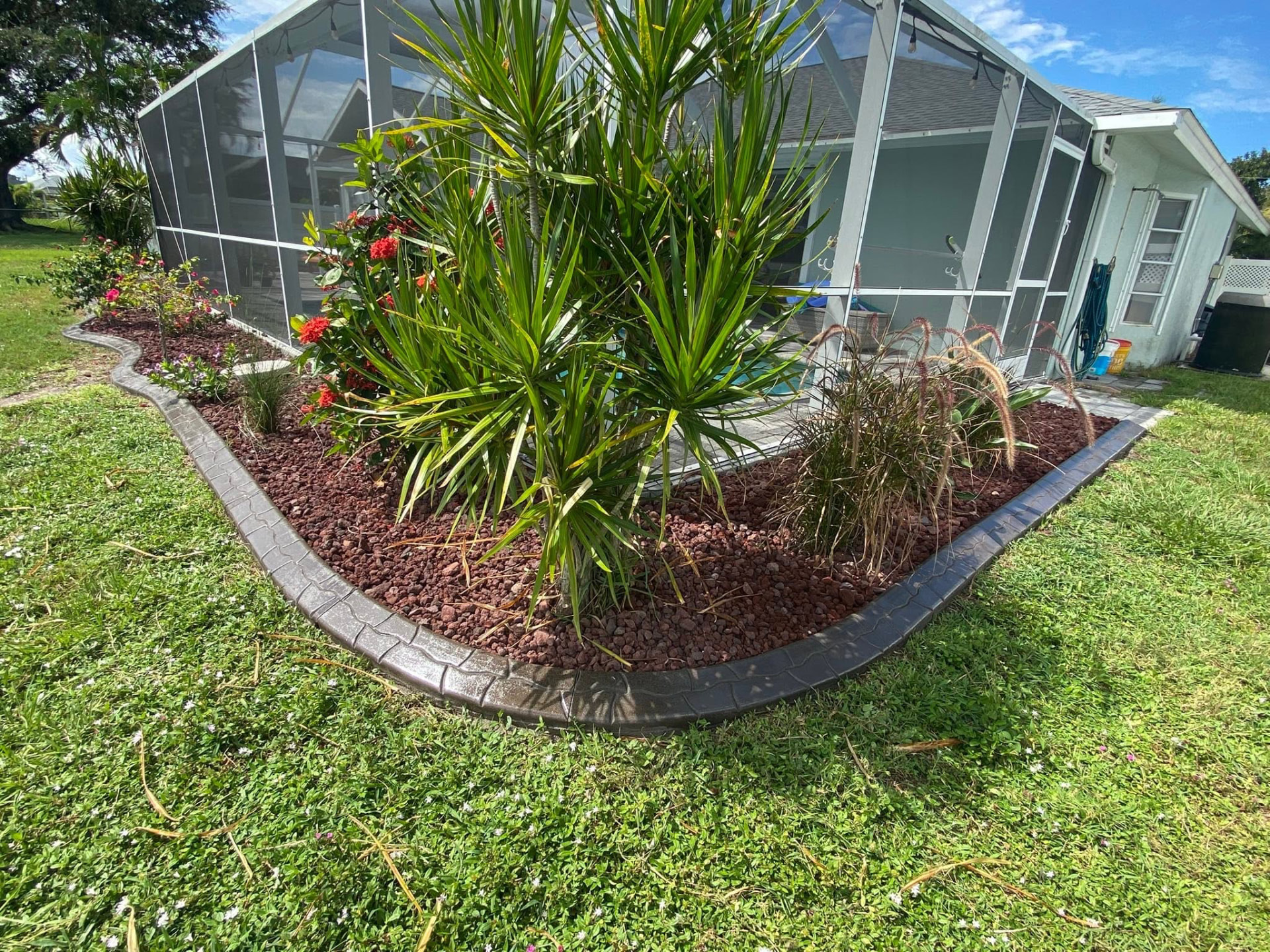 Dark stamped curbing around a red lava rock bed beside a pool cage